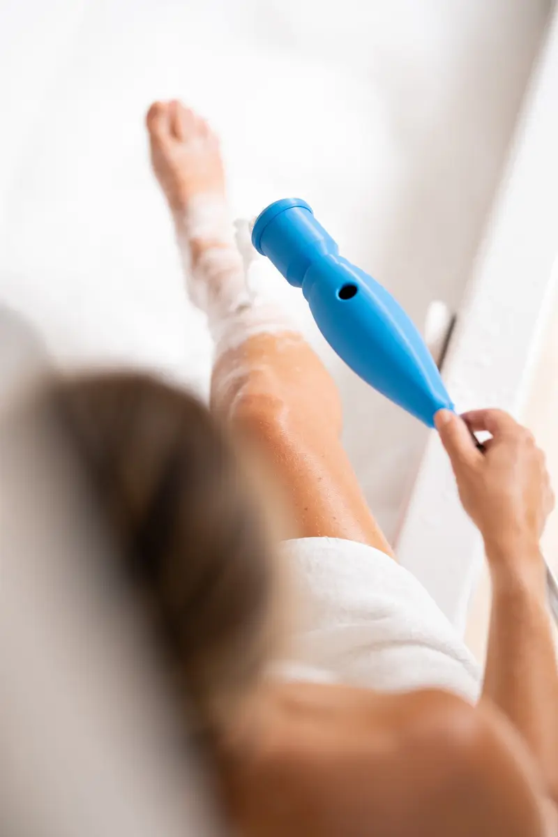 Frau in der Badewanne hält den blauen SchaumPo-Prototyp am Duschschlauch.